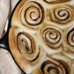 closeup of homemade caramel rolls in cast iron pan with towel alongside