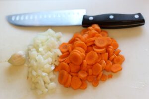 garlic clove and knife next to chopped onion and carrot