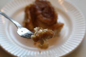 homemade caramel roll bite on fork with rest of roll on plate behind