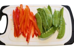 julienned red pepper next to snow peas on cutting board