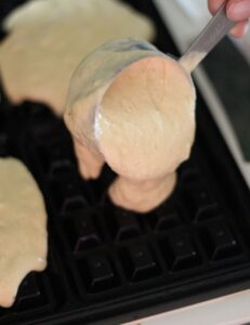pouring the dairy-free waffle batter into waffle iron using a measuring cup
