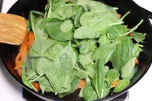 spinach in cast iron pan on top of red pepper and snow peas