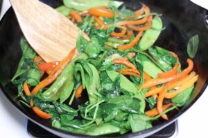 wilted spinach with red pepper and snow peas in cast iron pan and wooden spoon on side