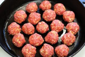 raw barbeque meatballs placed in single layer of cast iron pan