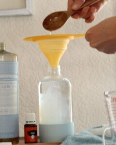 pouring castile soap into funnel on top of glass spray bottle