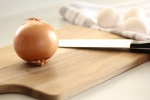 onion on a cutting board with a knife.  eggs shown in background.