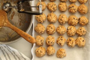 peanut butter energy balls on parchment lined baking sheet next to empty mixing bowl