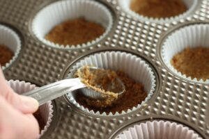 pressing graham cracker crust into muffin tin liners