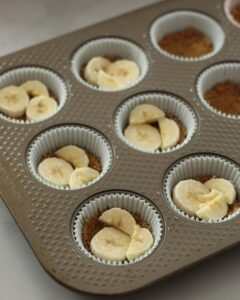 sliced bananas on top of graham cracker crust in muffin tin