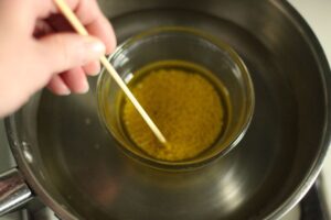 stirring olive oil and beeswax with wooden skewer as it heats in saucepan with water