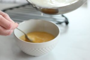 tempering eggs with hot mixture in saucepan pouring into whisked eggs in bowl