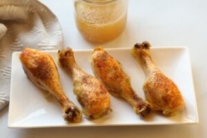 4 chicken legs on platter with jar of broth alongside