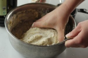 woman's hand kneading homemade pizza dough in mixing bowl
