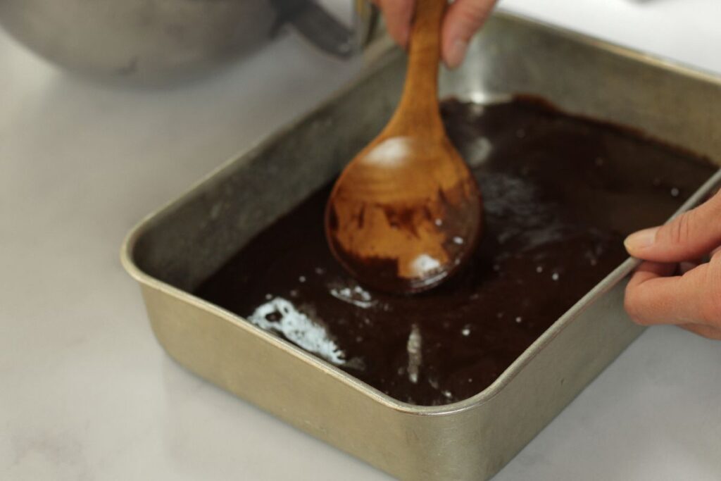 spreading gf brownie batter into pan with wooden spoon