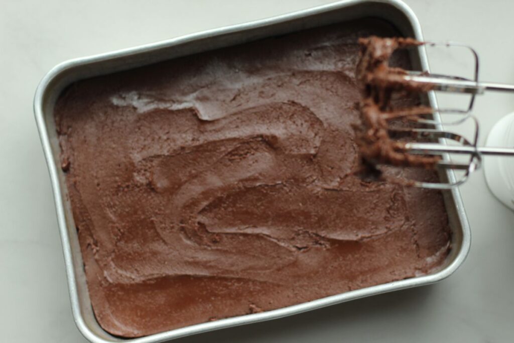 frosted gluten free brownies in pan next to hand mixer