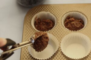 scooping grain free zucchini batter into muffin lined cups
