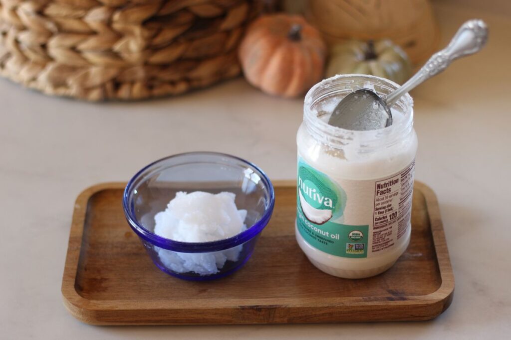 coconut oil scooped into a small glass dish next to the jar with a spoon inside