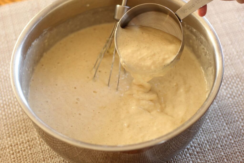 fluffy pancake batter in mixing bowl with a measuring cup scooping out batter