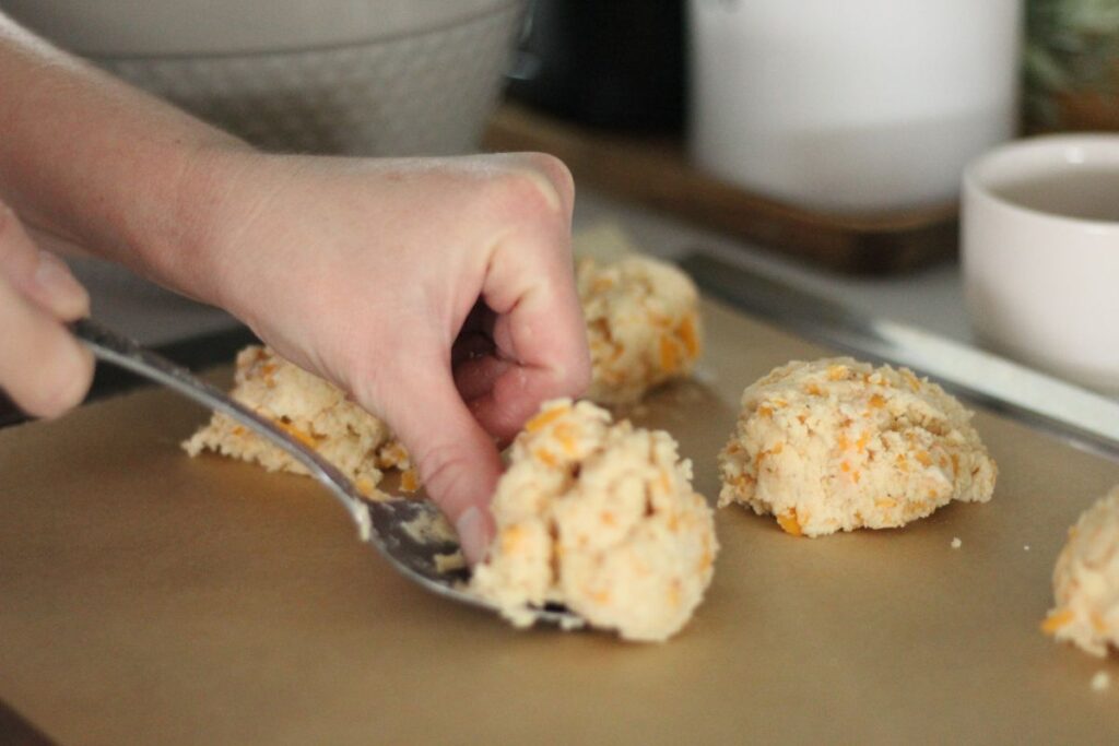 hand scooping homemade Red Lobster biscuit dough onto baking sheet lined with parchment paper