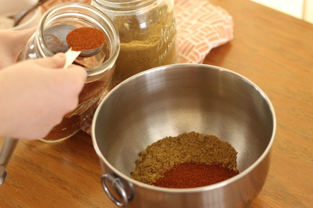 hand measuring smoked paprika into mixing bowl