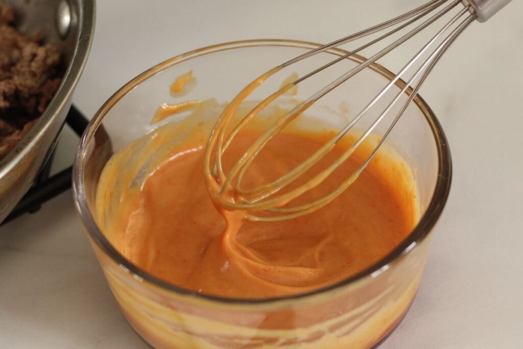 special sauce for cheeseburger pizza in a small glass bowl with a whisk