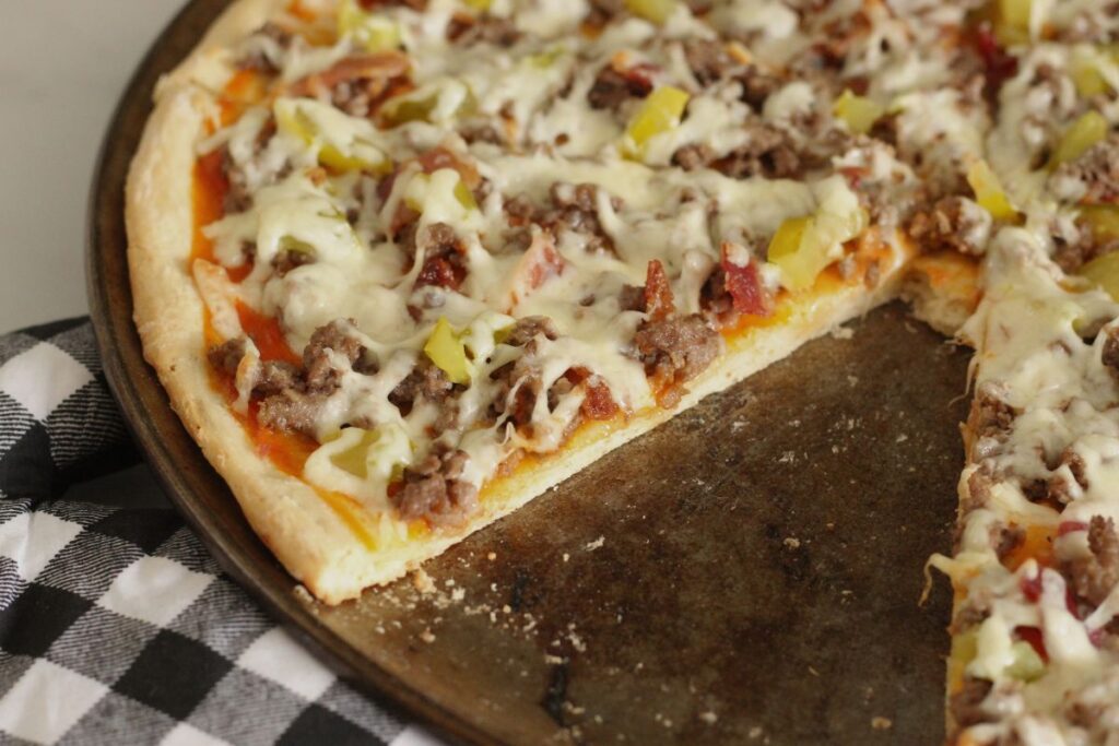 finished cheeseburger pizza on pizza pan with slice removed