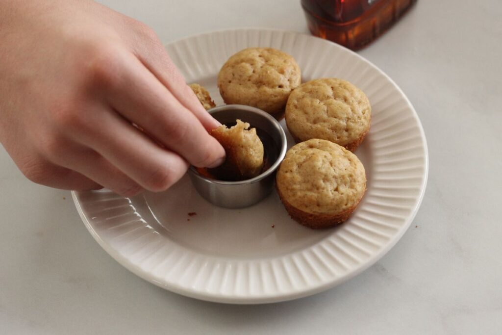 hand dipping a mini pancake muffin in syrup