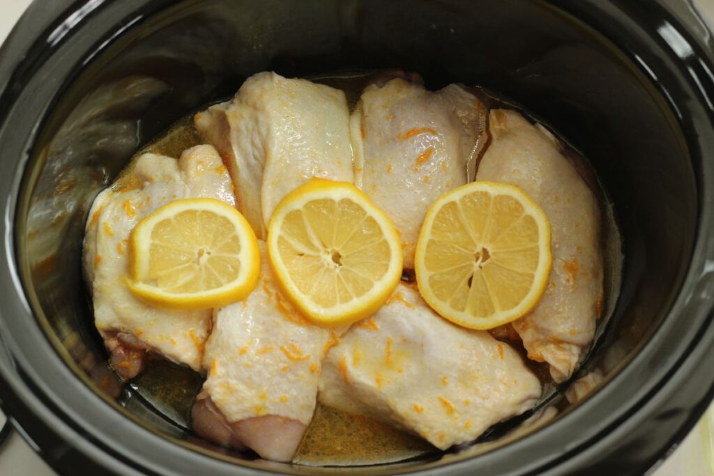 citrus & herb chicken thighs in crock pot with lemon slices on top