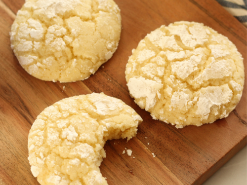 lemon crinkle cookies on wooden cutting board with a bite taken out of one of the cookies