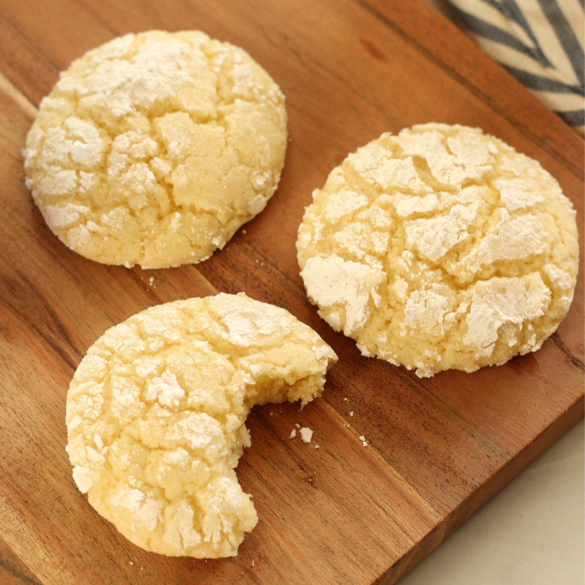 lemon crinkle cookies on wooden cutting board with a bite taken out of one of the cookies