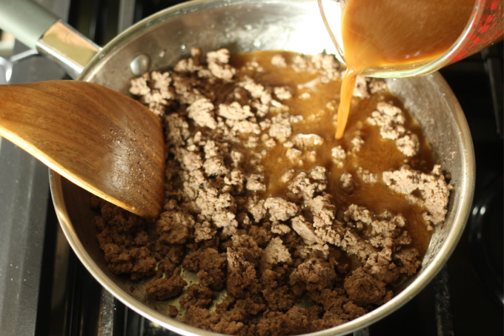 pouring sauce ingredients of beef & broccoli stir fry into skillet with browned ground beef