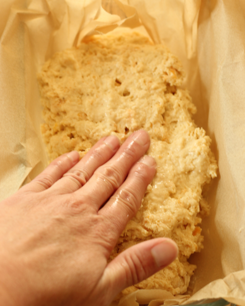 wet hand spreading batter of garlic cheesy quick bread into parchment lined bread pan