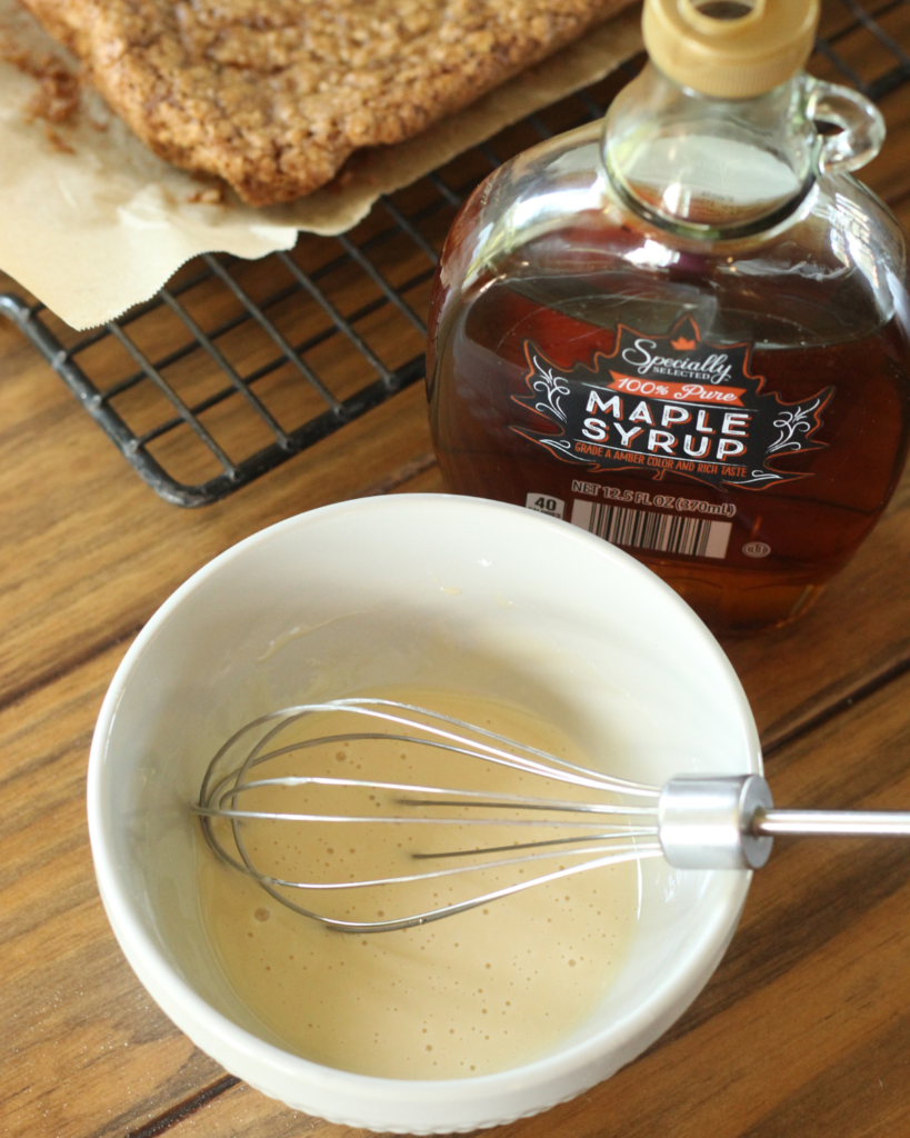 glaze in bowl with whisk. next to bottle of maple syrup.